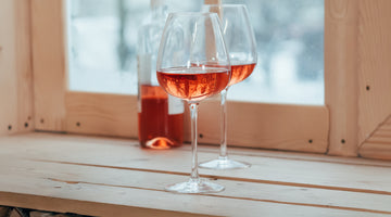 Zwei Weingläser mit Roséwein auf einer Holzfensterbank.