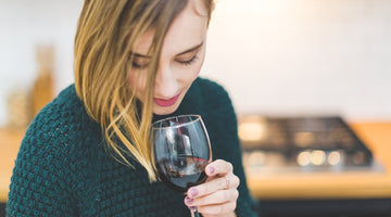 Frau mit grünem Pullover schaut in ein Glas Rotwein