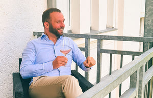 Robert Hesse trägt ein blaues Hemd, trinkt ein Glas Wein und lacht.