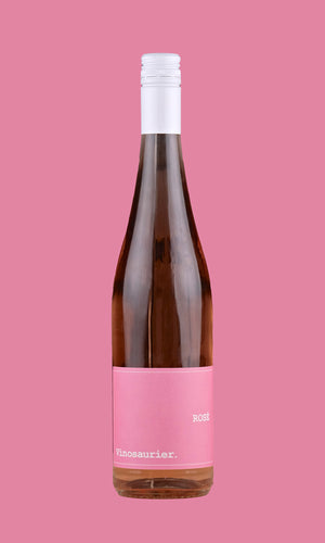 Eine Flasche Vinosaurier rosé vor einem rosafarbenen Hintergrund. Die Flasche ist durchsichtig, sodass der Roséwein direkt zu sehen ist. Das Etikett ist rosa mit weißer Schrift. Auch der Verschluss ist weiß.