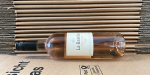 Das Bild zeigt eine Flasche La Bastille Rosé Wein, die auf einem Stapel gefalteter Pappkartons liegt.