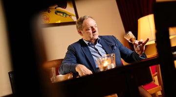 Auf dem Bild ist Stefan Maas zu sehen. Er sitzt im Anzug in einer urigen Location und schaut nachdenklich in ein Glas Wein.