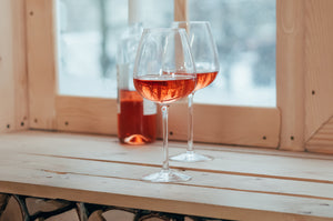 Zwei Weingläser mit Roséwein auf einer Holzfensterbank.