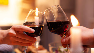 Auf dem Bild sind zwei Hände zu sehen, die mit einem Glas trockenen Rotwein anstoßen.