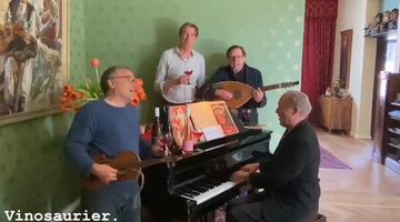 Auf dem Bild ist eine Gruppe Männer zu sehen. Einer von ihnen sitzt am Klavier. Eine weiterer spielt Gitarre. Sie trinken Vinosaurier Rosé und musizieren. 