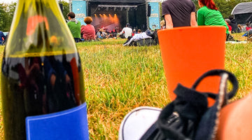 Auf dem Bild ist eine Flasche Vinosaurier blau zu sehen. Daneben im Bild steht ein Weinkelch aus Plastik und ein Fuß ist auch zu sehen. Das Foto wurde auf einem Open-Air-Konzert aufgenommen.