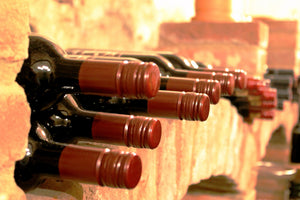 Das Bild zeigt Rotweine, die in einer Wand aus Ziegeln gelagert werden. Zu sehen ist nur der obere Teil der Flasche.