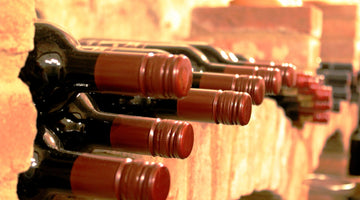 Das Bild zeigt Rotweine, die in einer Wand aus Ziegeln gelagert werden. Zu sehen ist nur der obere Teil der Flasche.