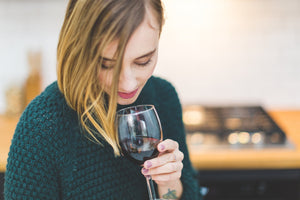 Frau mit grünem Pullover schaut in ein Glas Rotwein