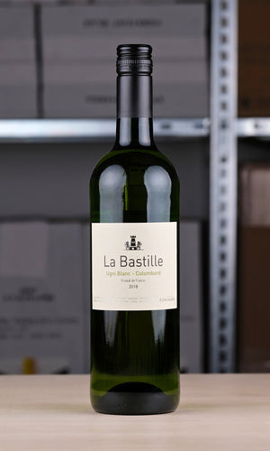 Eine Flasche La Bastille Blanc vor einem Regal fotografiert. Die Flasche ist grün, das Etikett ist weiß. Darauf steht mit schwarzer Schrift: "La Bastille". Darunter in grüner Schrift: "Ugni Blanc - Colombard".