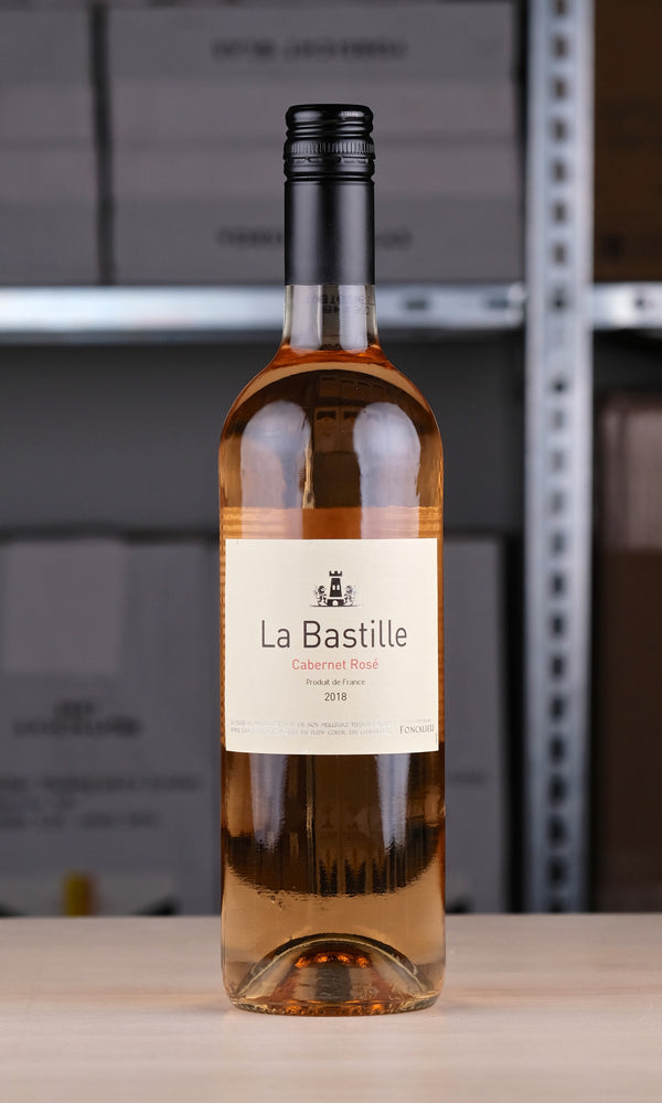 Eine Flasche La Bastille Rosé vor einem Regal fotografiert . Die Flasche ist durchsichtig, das Etikett ist weiß. Darauf steht mit schwarzer Schrift: "La Bastille". Darunter in rosa Schrift: "Cabernet Rosé.