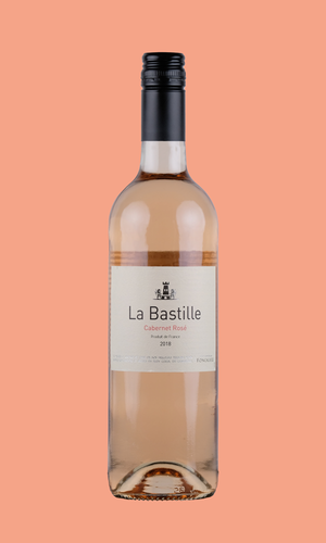 Eine Flasche La Bastille Rosé auf lachsfarbenem Hintergrund. Die Flasche ist durchsichtig, das Etikett ist weiß. Darauf steht mit schwarzer Schrift: "La Bastille". Darunter in rosa Schrift: "Cabernet Rosé.