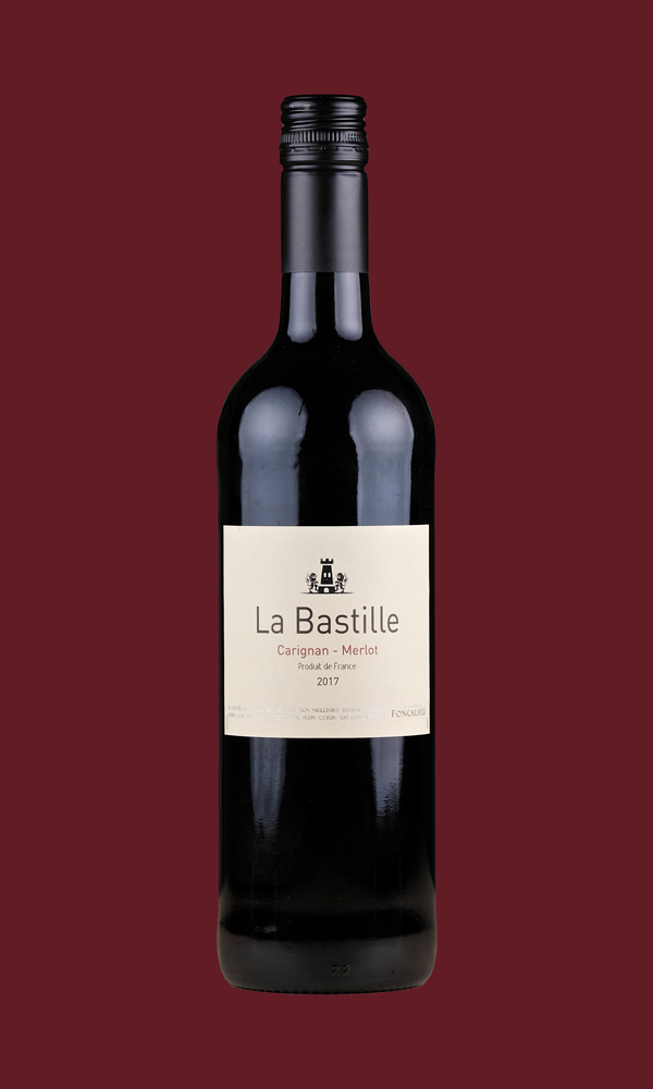 Eine Flasche La Bastille Rouge auf dunkelrotem Hintergrund. Die Färbung der Flasche ist wegen der dunklen Farbe des Weins nicht zu erkennen, das Etikett ist weiß. Darauf steht mit schwarzer Schrift: "La Bastille". Darunter in dunkelroter Schrift: "Carignan - Merlot"