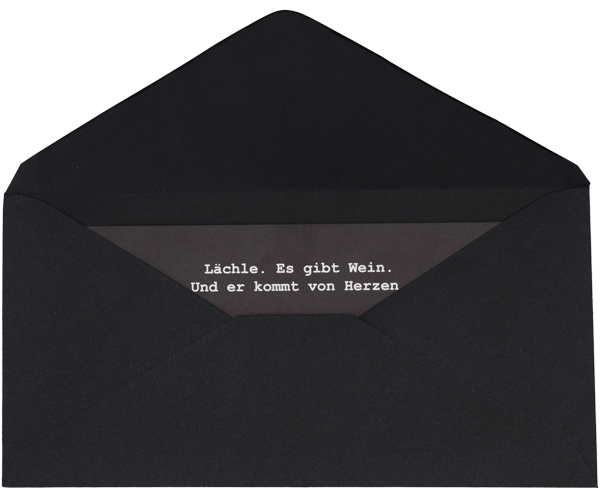 Ein schwarzer geöffneter Briefumschlag, in dem ein ebenfalls schwarzes Papier steckt. Auf dem Papier steht in weißer Schrift: "Lächle. Es gibt Wein. Und er kommt von Herzen."